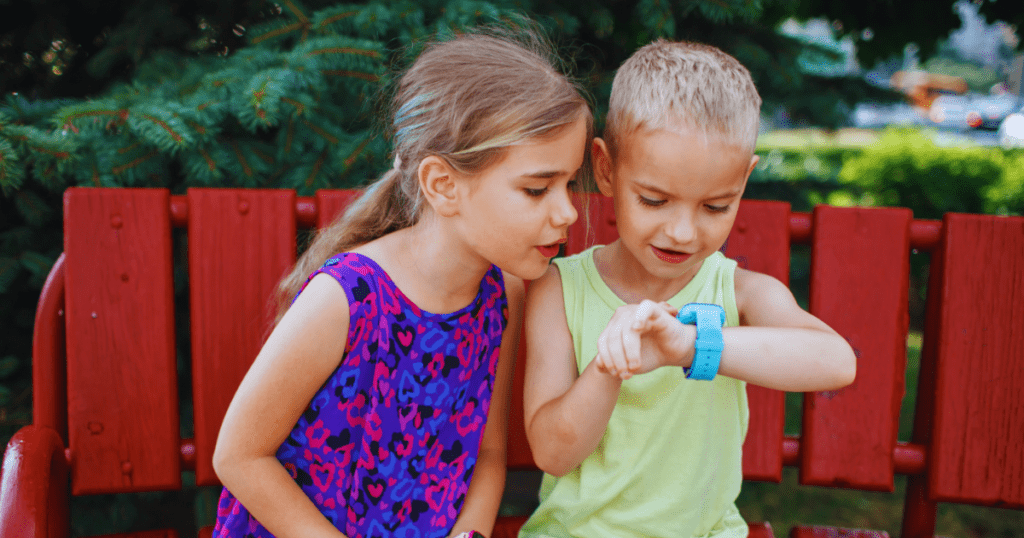 Egy kislány és egy kisfiú egymás mellett ülve nézik a kisfiú okosóráját