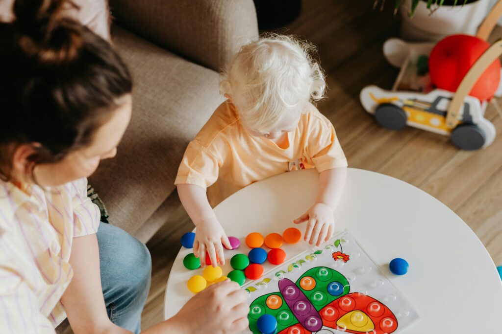 Egy 4 éves kisgyerek egy színes társasjátékkal játszik, mellette az anyukája